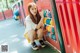 A young woman sitting on the ground in front of a playground.